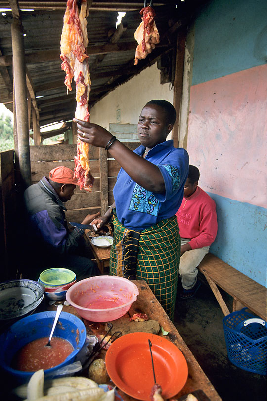 At a local Hoteli a woman cuts meat <p>to cook Nyama choma, grilled meat, often served <p>with cabbage, boiled rice and a spicy tomato sauce.