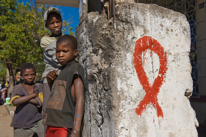 Street children standing at a pillar with a <p>painted HIV/AIDS ribbon, Quelimane Mozambique