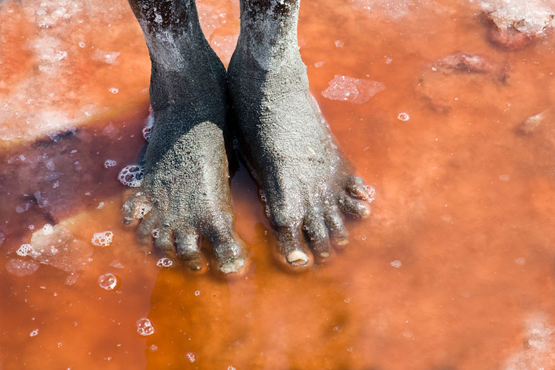 The feet of a salt miner <p>standing in the salt water of Lake Natron