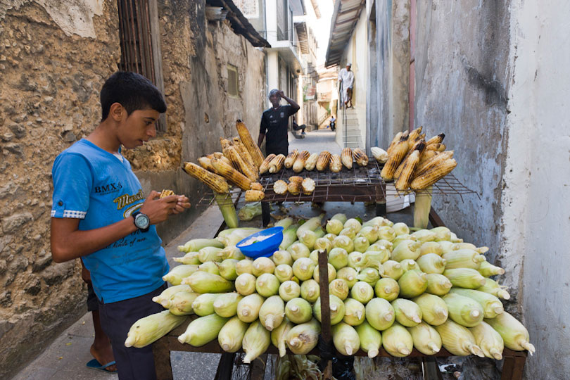 Boy buying grilled maize cobs from a food stand,<p> Stone Town, Zanzibar, Tanzania