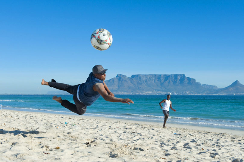 Young men playing football on the beach in Bloubergstrand,<p> Cape Town, South Africa