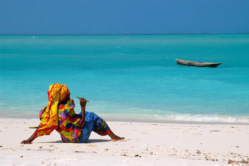Woman in traditional dress rests <p>on the beach of Zanzibar